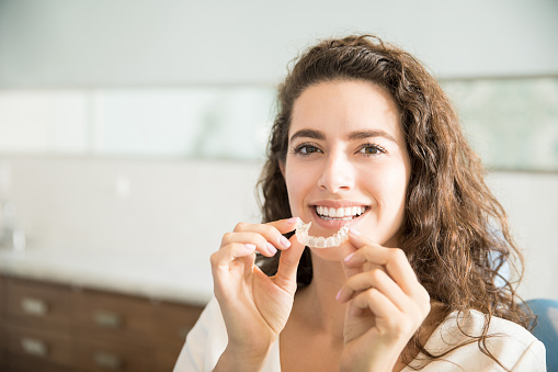 Woman holding clear aligner in front of mouth at Karl Hoffman Dentistry in Lacey, WA