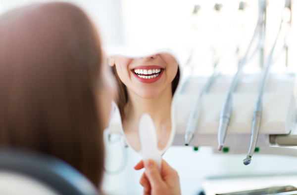 Woman looking at her smile in a mirror after restorative dentistry at Karl Hoffman Dentistry in Lacey, WA 